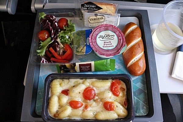 a tray of airplane food featuring gnocchi in a cream sauce with cherry tomatoes