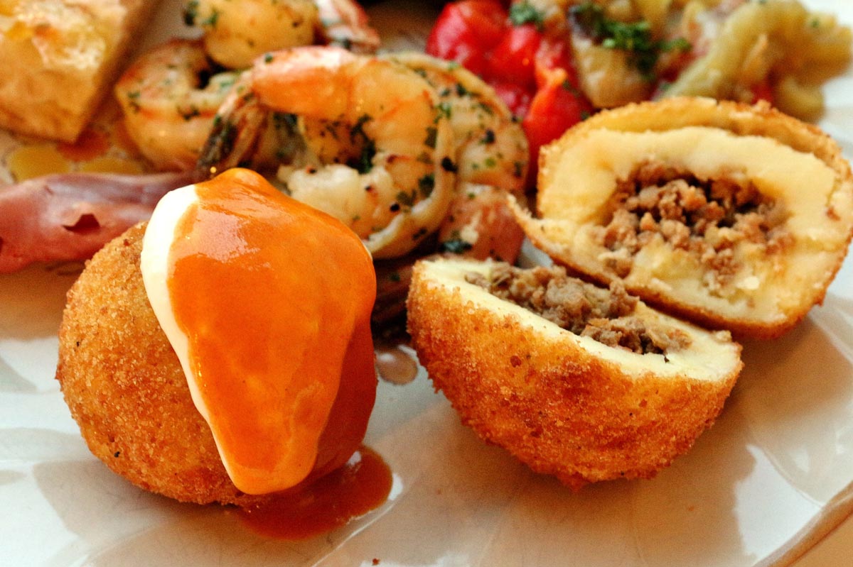 A plate of tapas, including 2 fried potato bombas with sauce, shrimp, and veggies.