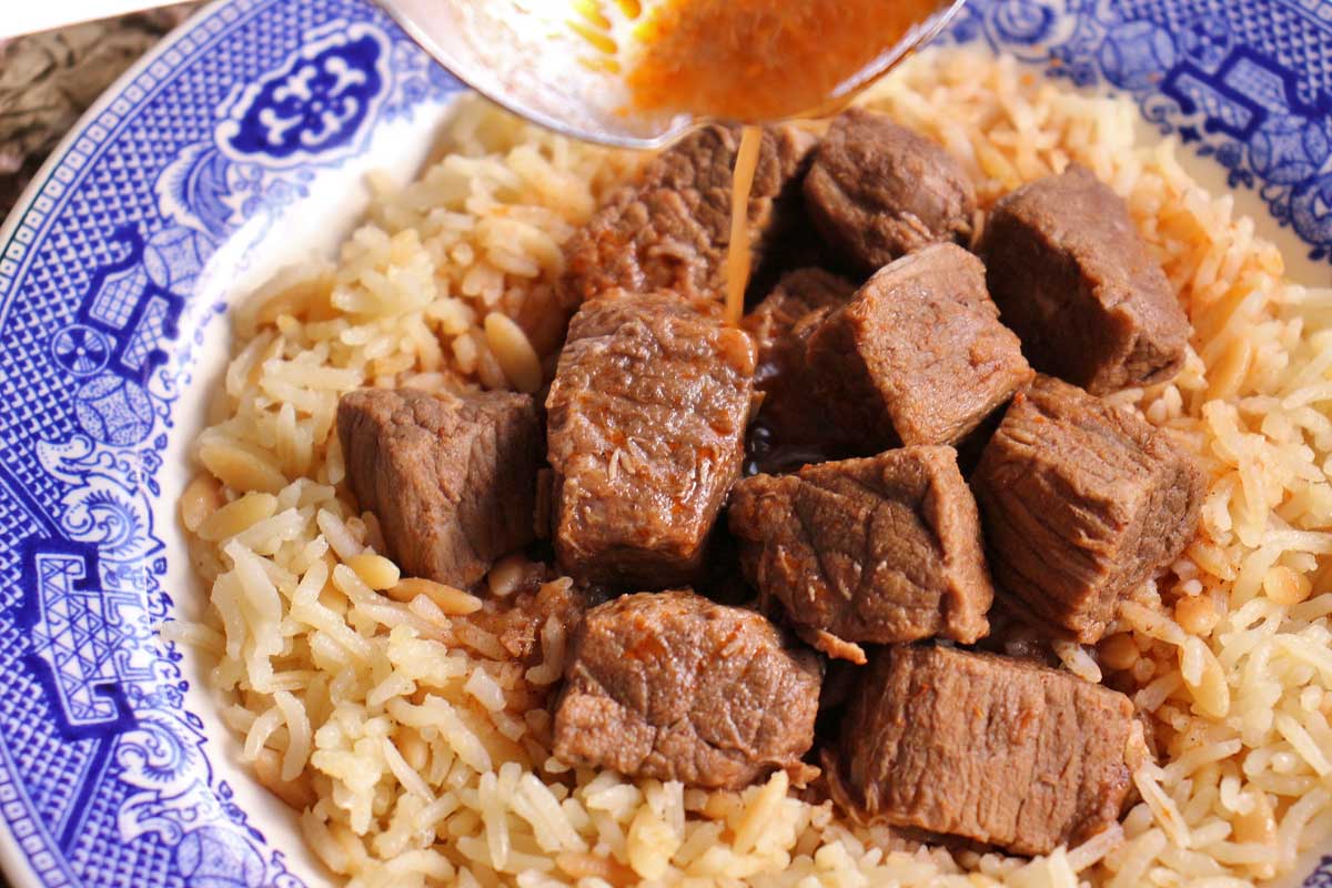 Closeup of tas kebab served over rice pilaf with stew liquid spooned over the top.