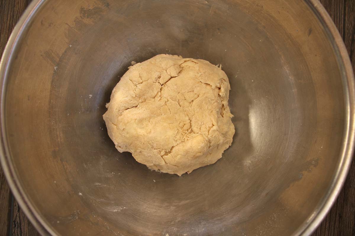 A flattened ball of homemade pie dough in a metal mixing bowl.