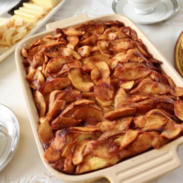Baked apple french toast casserole on a table with teacups and a cheese platter.