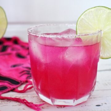 Closeup of a bright pink prickly pear margarita garnished with a lime slice.