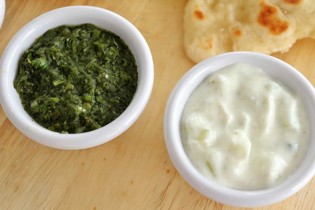 A close up of the Coriander Chutney and Cucumber Raita in small cups.
