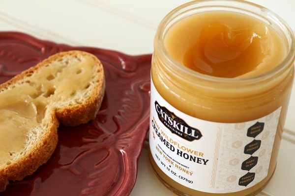 A close up of an opened jar of creamed honey with a piece of toast