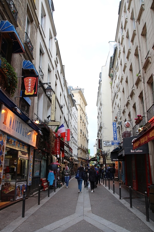 A narrow city street with people walking on a sidewalk