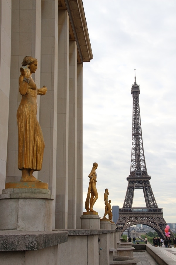 a row of gold statues in front of the Eiffel Tower