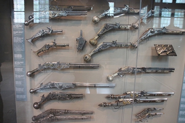 A bunch of different ancient guns in a museum display