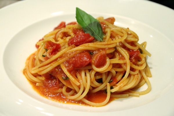spaghetti with a cherry tomato sauce and basil on a white plate
