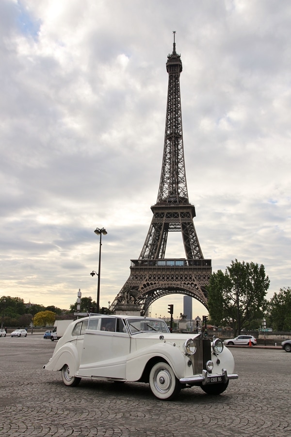 a white antique car in front of the Eiffel Tower