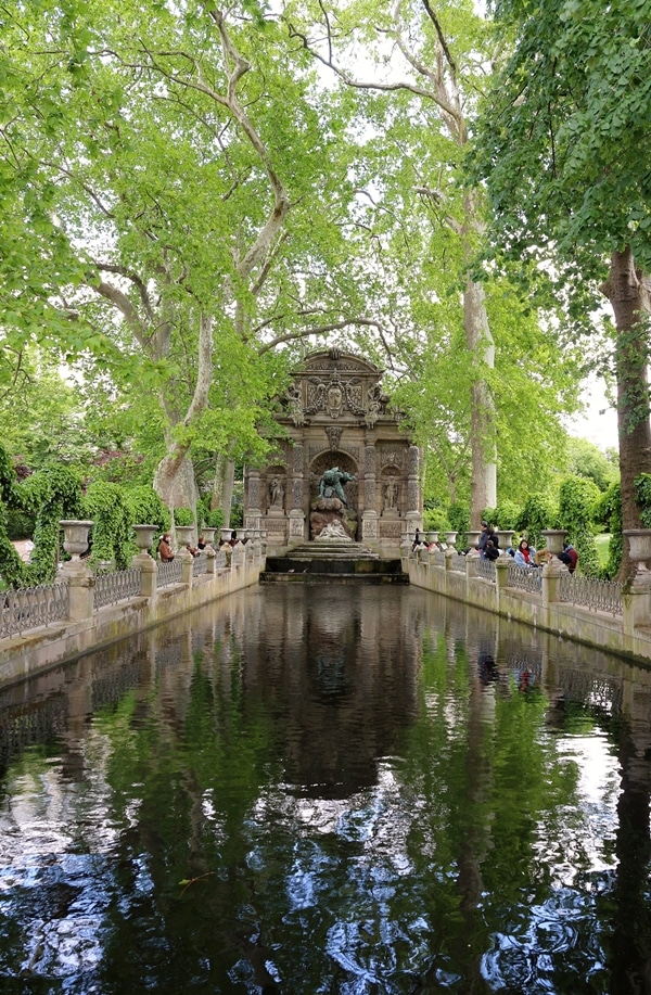 a long tree-covered fountain with a statue at the far end