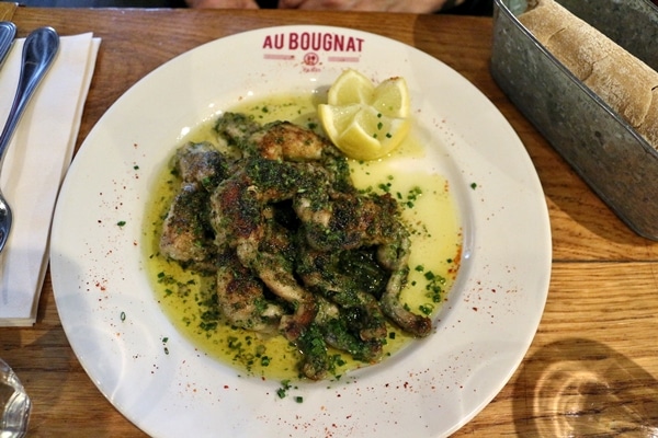a plate of frogs legs with a buttery sauce and parsley