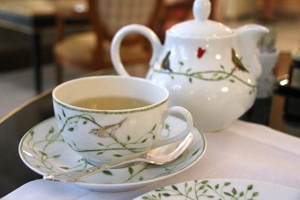 a tea cup with a tea pot behind it