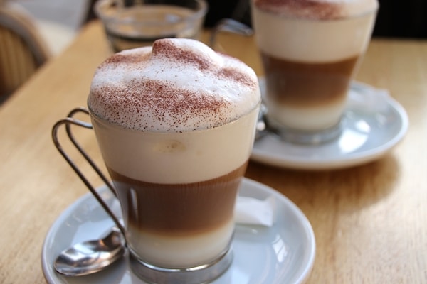 2 cappuccinos in glass mugs garnished with cocoa powder