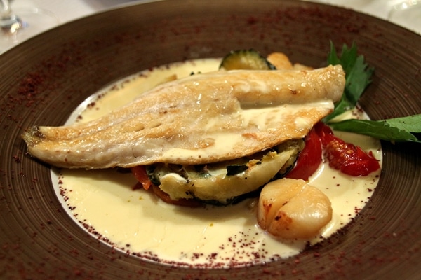 a fish fillet with scallops and vegetables with a white sauce