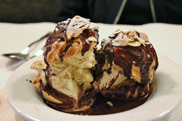 profiteroles filled with ice cream and topped with chocolate sauce on a white plate