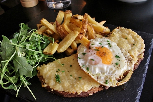 a croque madame sandwich with fries and salad on a black surface