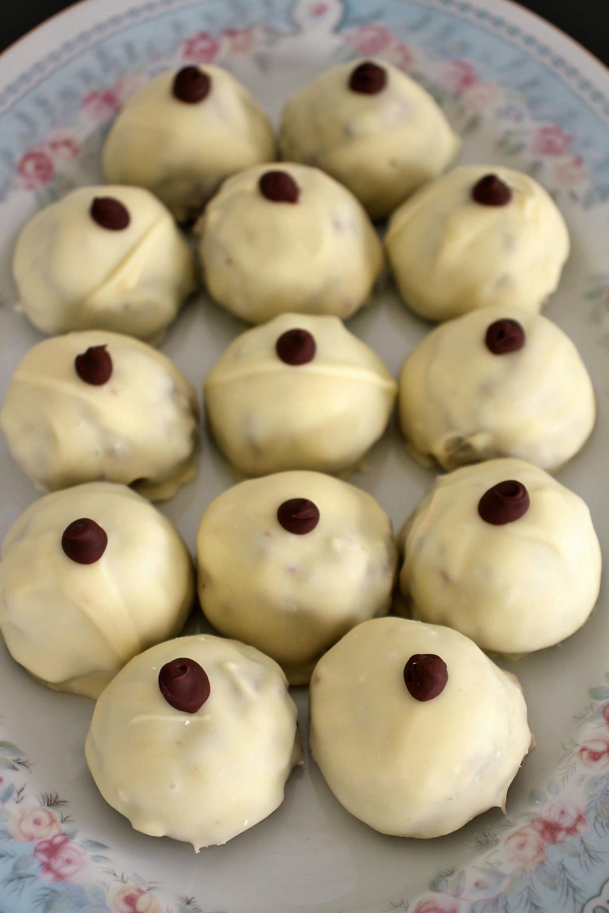 A platter of white chocolate covered truffles with a dark chocolate dot on top.