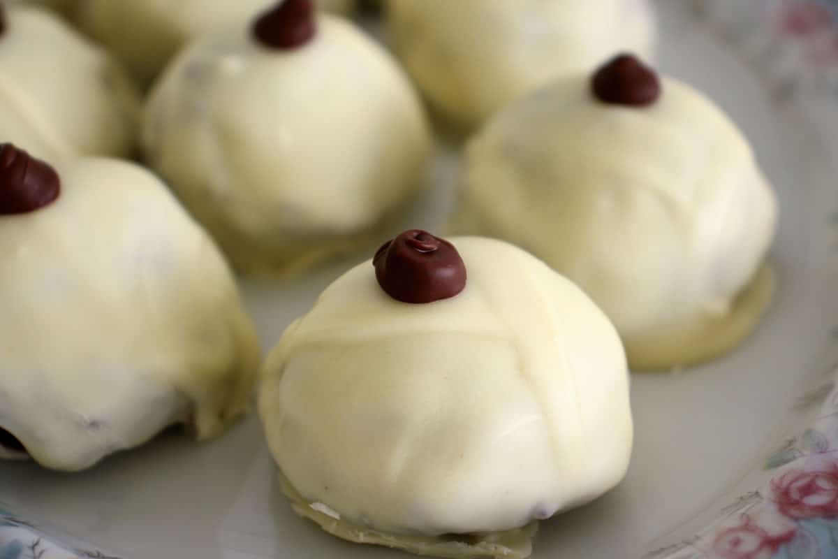 Close up of white chocolate covered truffles with a dark chocolate dot on top.