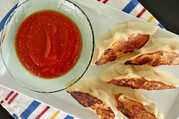 Pan-fried dumplings on a white plate with a dish of marinara sauce for dipping