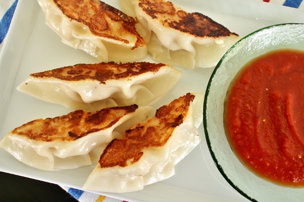 Pan-fried chicken parmesan dumplings on a white plate with marinara sauce for dipping