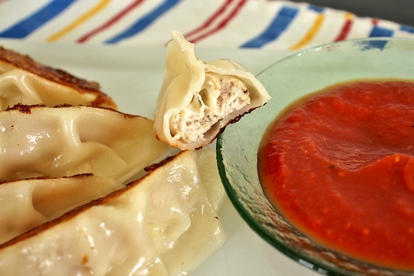 a dumpling with a bite taken out, resting on the edge of a dipping sauce bowl