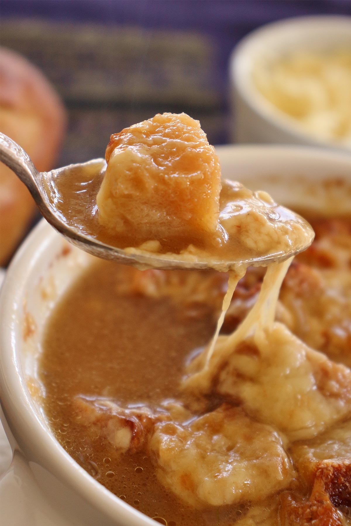 closeup of a spoonful of French onion soup with stretching melted cheese