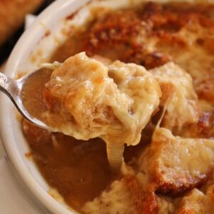 closeup of a spoonful of French onion soup with a crouton and melted cheese