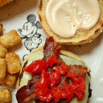 A cheeseburger with bacon and pickled cherry peppers on a white plate.