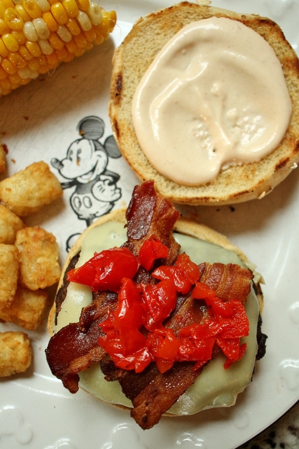 An open-faced cheeseburger with crispy bacon and cherry peppers on top.