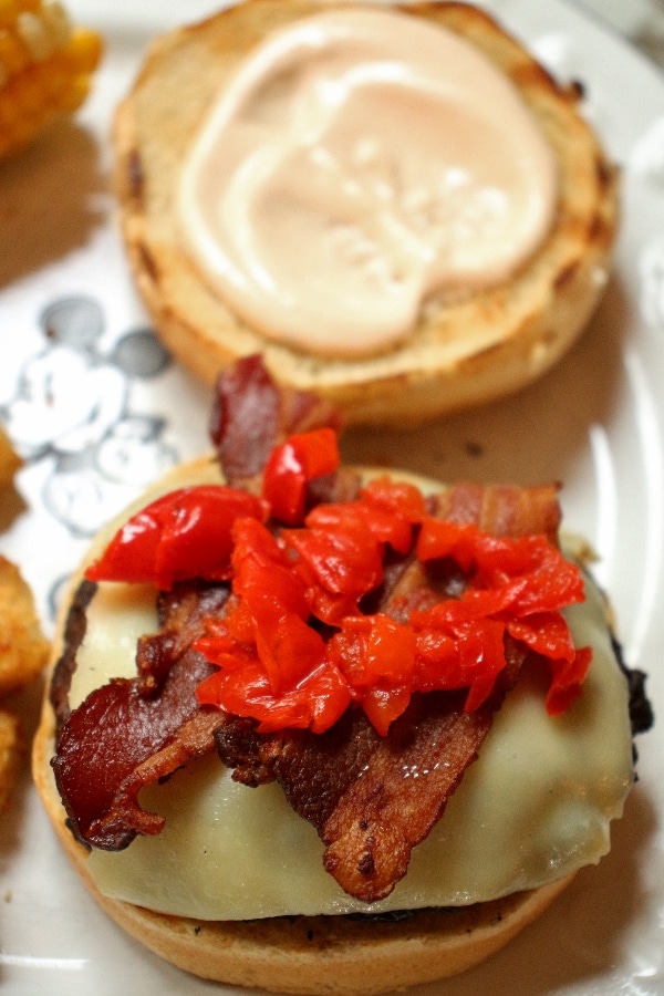 Closeup of an open-faced cheeseburger with bacon and red cherry peppers.