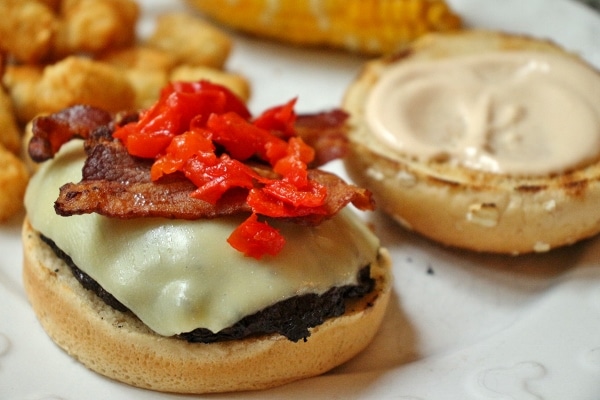 Closeup of a cheeseburger with bacon and cherry peppers on top.