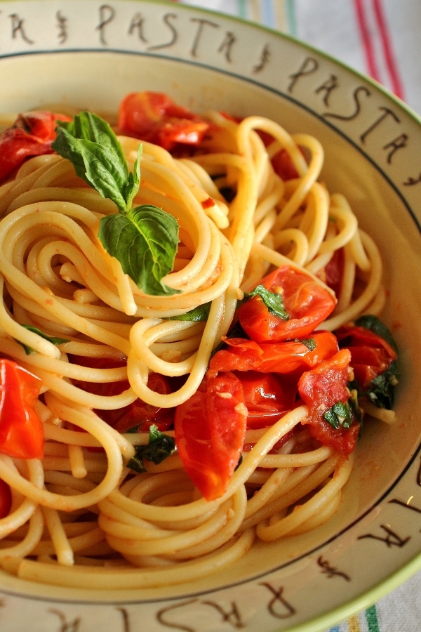 side view of spaghetti with cherry tomato and basil sauce in a wide bowl