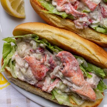 Closeup of two lobster rolls with lemon wedges on a white platter.