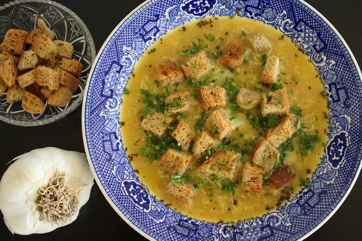 Czech garlic soup, a bowl of croutons and head of garlic next to the soup.