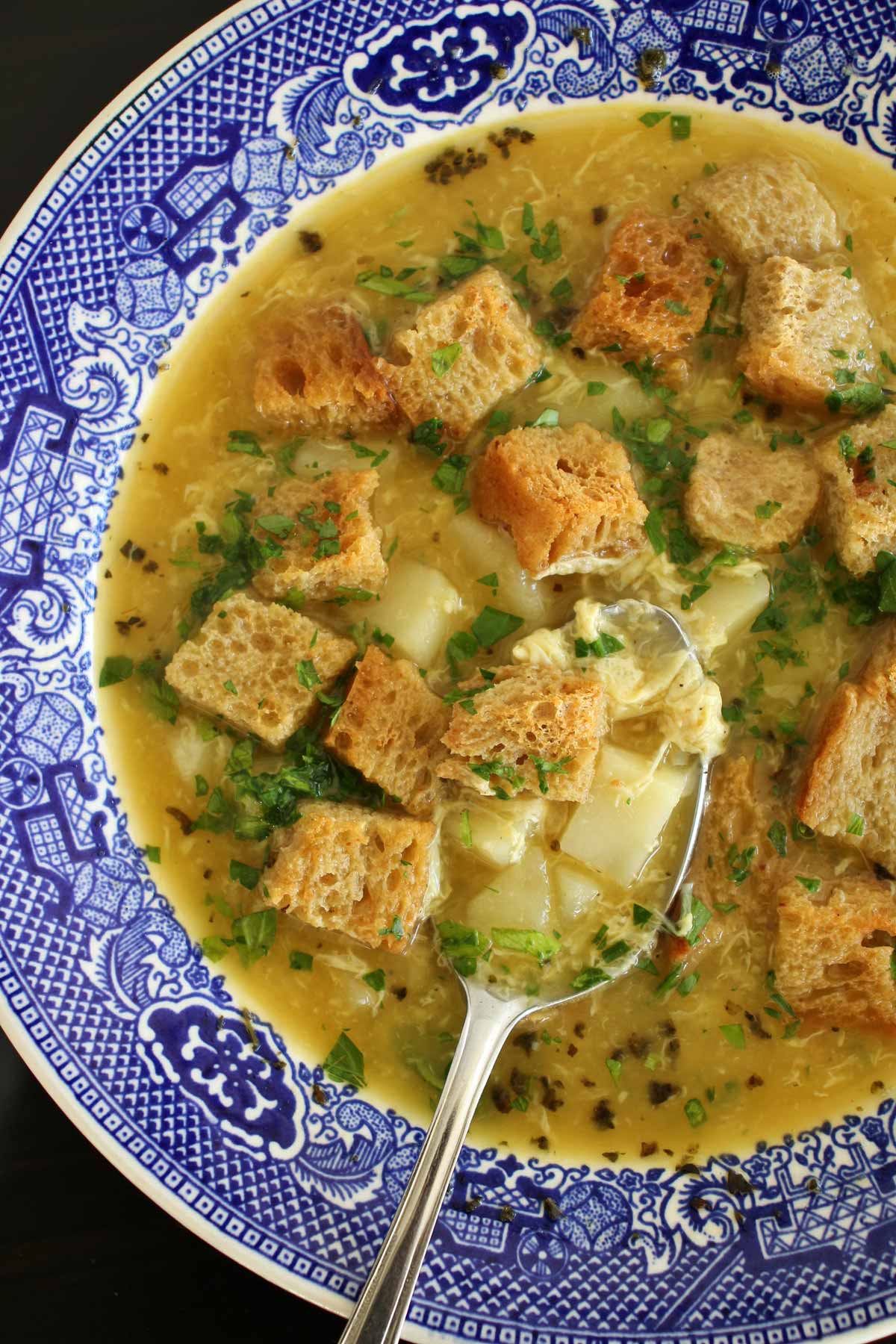 Czech garlic soup topped with rye croutons in a blue and white bowl.