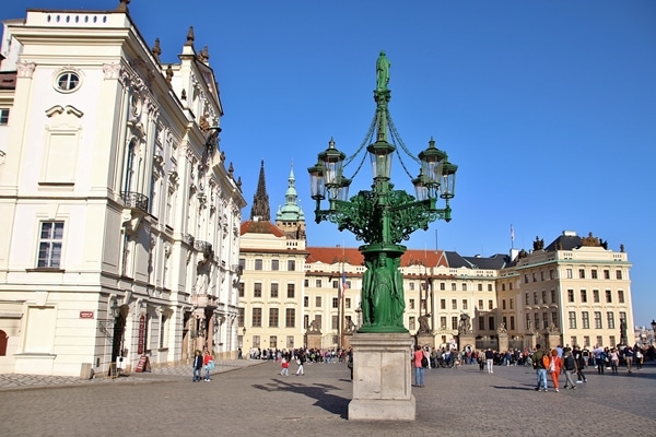 A large green street light in front of a big city square with buildings