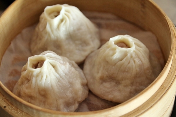 3 steamed soup dumplings in a bamboo steamer basket