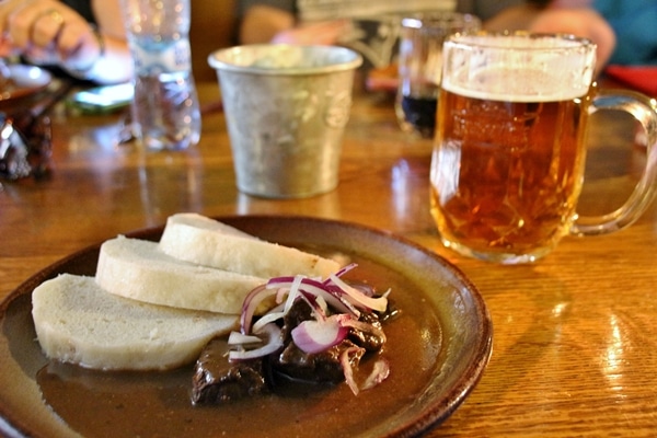 a plate of beef goulash next to a glass of beer