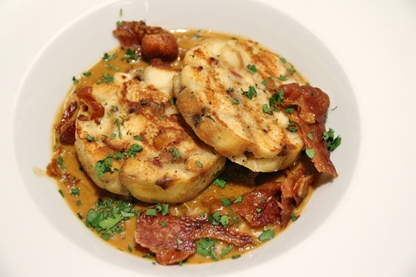 2 bread dumplings with bacon and a brown sauce in a white bowl