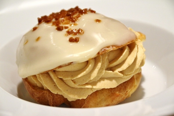 side view of a caramel profiterole on a white plate