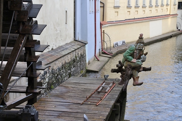 closeup of a watermill and statue of a creature on a stream