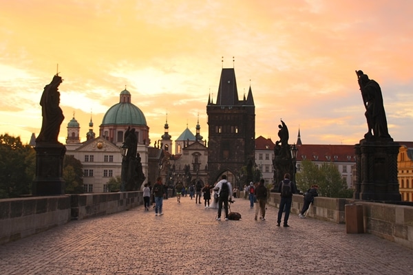 A group of people walking on Charles Bridge at sunrise