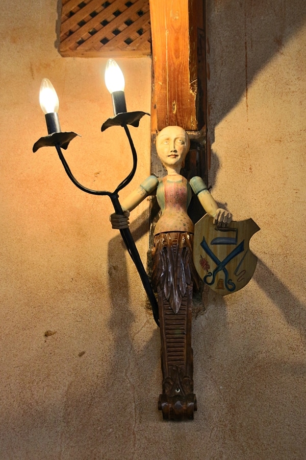 a wooden carving on a wall holding up a light fixture