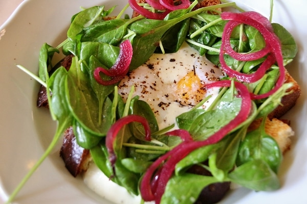 a poached egg with baby spinach, and pickled onions on a white plate