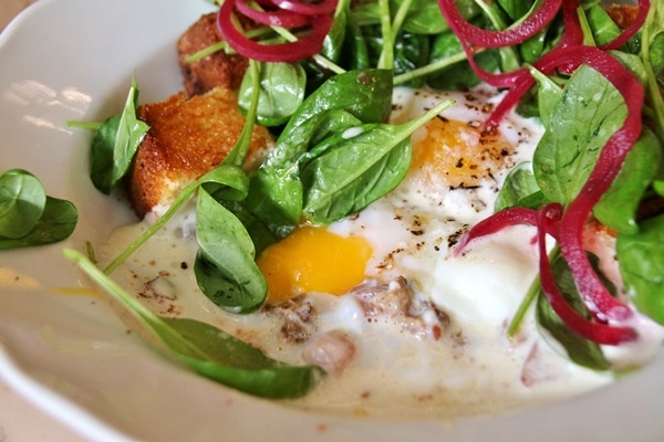 closeup of a poached egg with bacon lardons and baby spinach