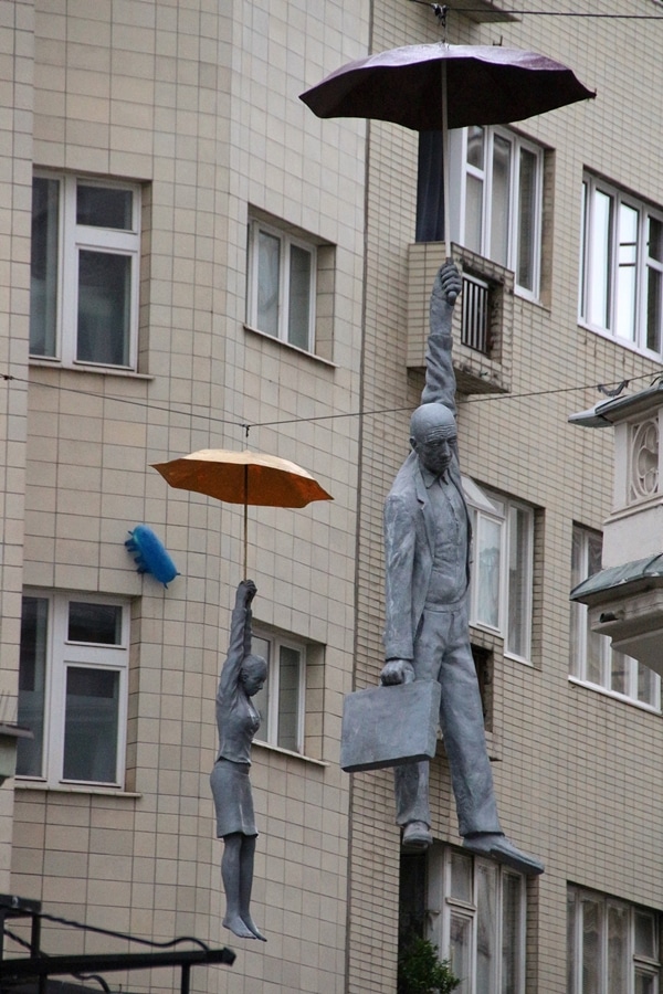 2 statues of people hanging from umbrellas