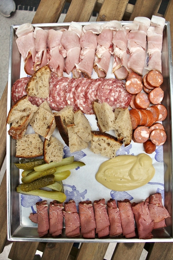 a Czech charcuterie plate with sliced cured meats, ham, sausage, bread, pickles, and mustard