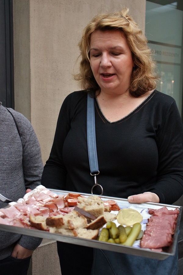 female tour guide holding up a platter of cured meats, bread, and mustard