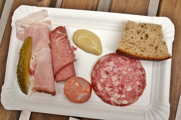 selection of ham and cured meats, bread, and mustard on a white plate