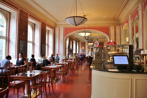 interior of the cafe section of Cafe Louvre in Prague with many tables and pink walls